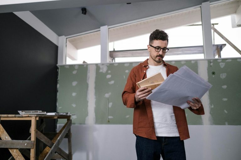 A focused adult male architect examines construction plans indoors, showcasing project management.