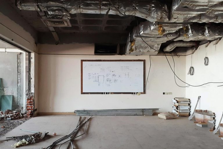 An empty room under construction with exposed ceiling ducts and a whiteboard.